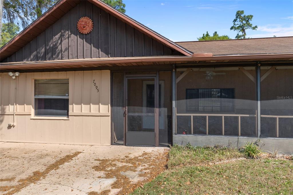 The exterior of a house features a screened-in porch, tan siding, and a sun decoration — 7095 W GREENWOOD LANE, CRYSTAL RIVER, FL