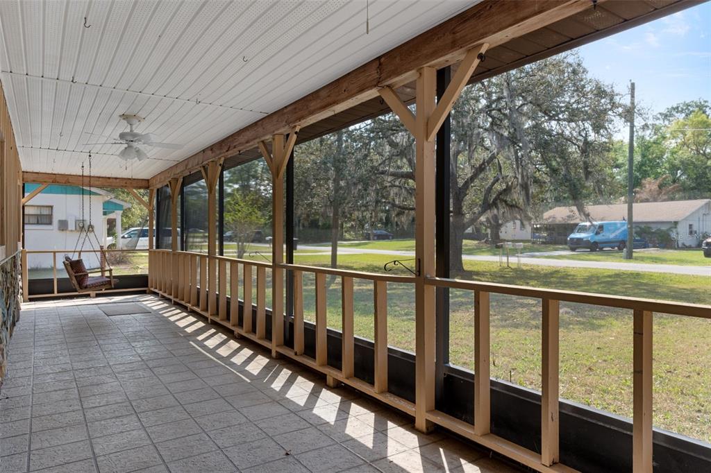 A screened-in porch features a tiled floor, a ceiling fan, and a wooden porch swing — 7095 W GREENWOOD LANE, CRYSTAL RIVER, FL