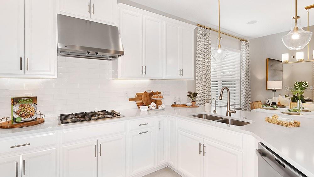 A bright kitchen features white cabinetry, a stainless steel range hood, and a quartz countertop — 5641 GINGHAM DRIVE, KISSIMMEE, FL