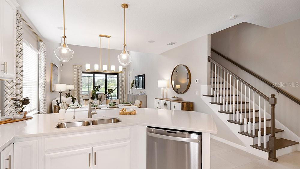 A kitchen island with a stainless steel sink overlooks a dining area and staircase — 5641 GINGHAM DRIVE, KISSIMMEE, FL