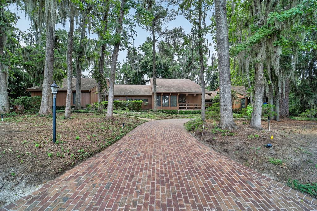 A brick driveway leads to a brown wood-sided house surrounded by trees with Spanish moss — 2411 SE 15TH STREET, OCALA, FL