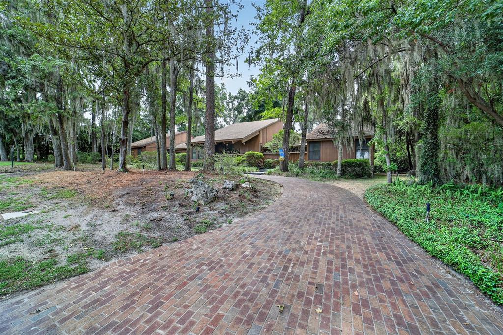A brick driveway leads to a brown wood-sided house surrounded by trees with Spanish moss — 2411 SE 15TH STREET, OCALA, FL