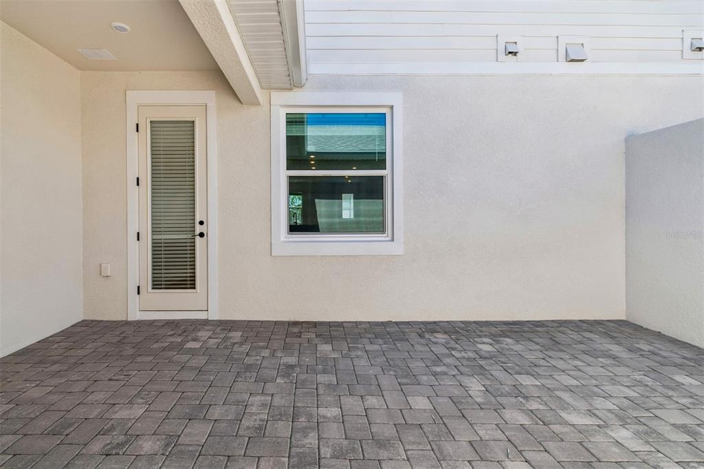 A covered patio features gray paver flooring, a glass-paneled door, and a single window — 8119 SEAFLOWER PARKWAY, BRADENTON, FL