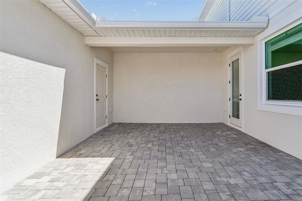 A covered patio with gray paver flooring, light-colored stucco walls, and two exterior doors — 8119 SEAFLOWER PARKWAY, BRADENTON, FL