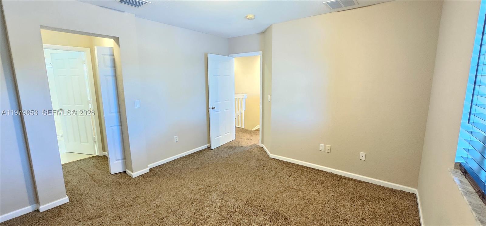 An empty bedroom features beige walls, brown carpeting, and two open white doors — 2014 Marsh Harbor Dr, Riviera Beach FL 33404, RIVIERA BEACH, FL