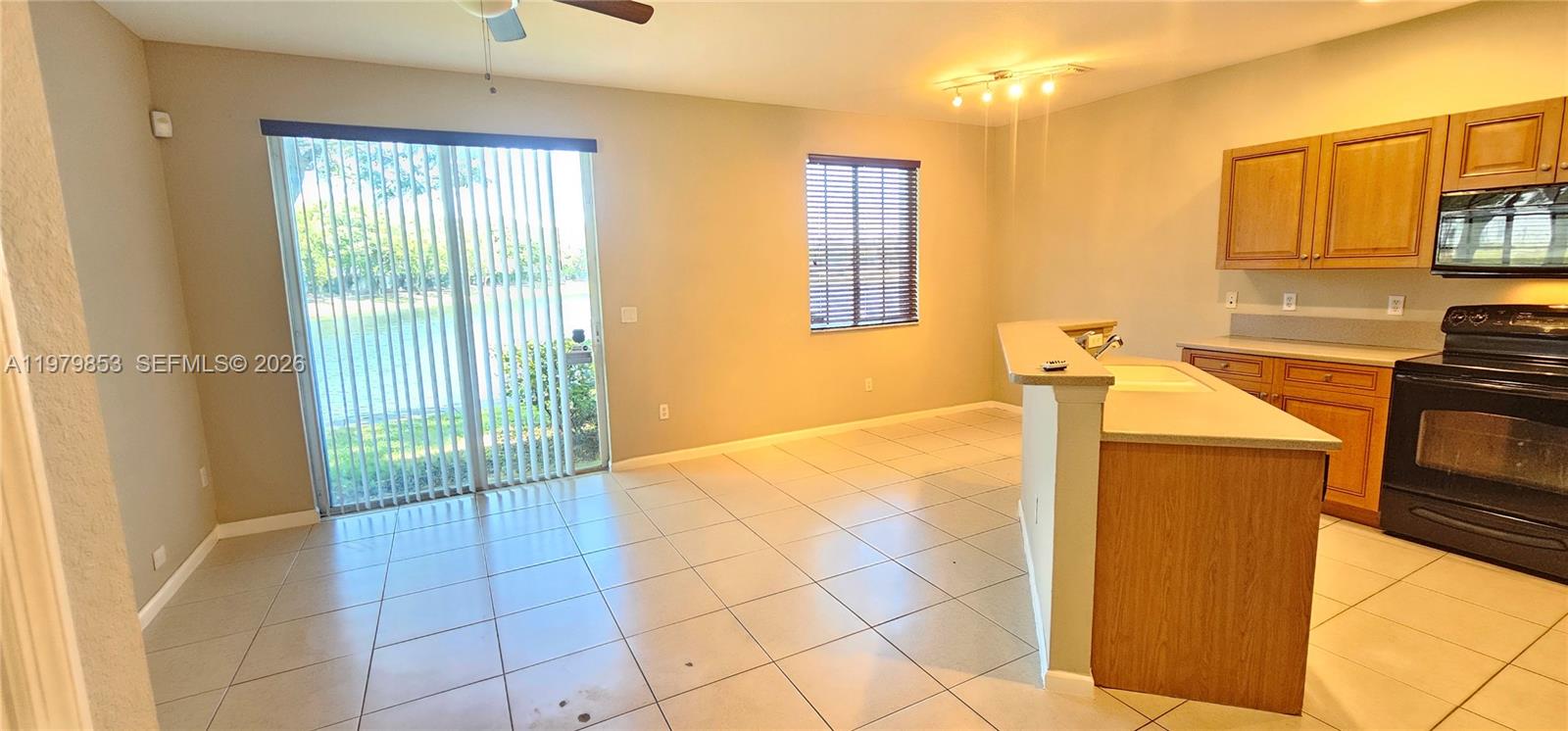 A kitchen with wood cabinets and tile flooring opens to a dining area with sliders — 2014 Marsh Harbor Dr, Riviera Beach FL 33404, RIVIERA BEACH, FL