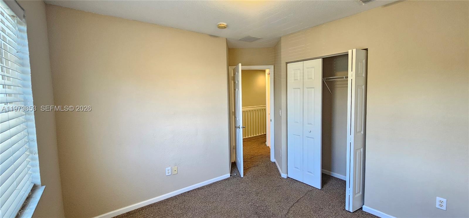 A bedroom features beige walls, brown carpet, a window with blinds, and an open closet — 2014 Marsh Harbor Dr, Riviera Beach FL 33404, RIVIERA BEACH, FL