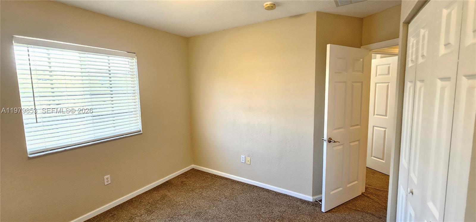 An empty bedroom features beige walls, brown carpet, a window with blinds, and two doors — 2014 Marsh Harbor Dr, Riviera Beach FL 33404, RIVIERA BEACH, FL