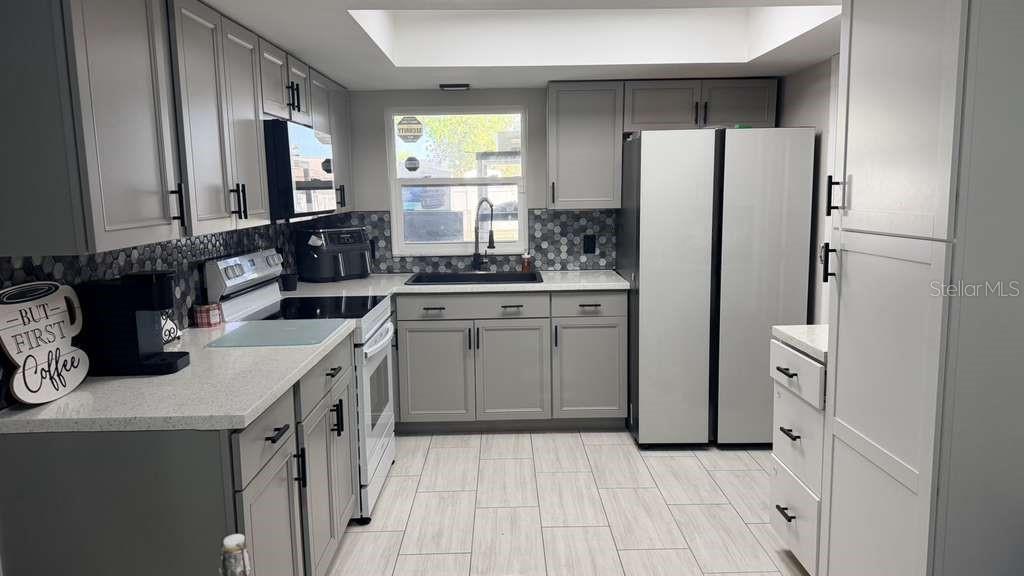 A kitchen features gray cabinets, white countertops, a hexagonal tile backsplash, and stainless steel appliances — 1420 MYRNA LANE, KISSIMMEE, FL