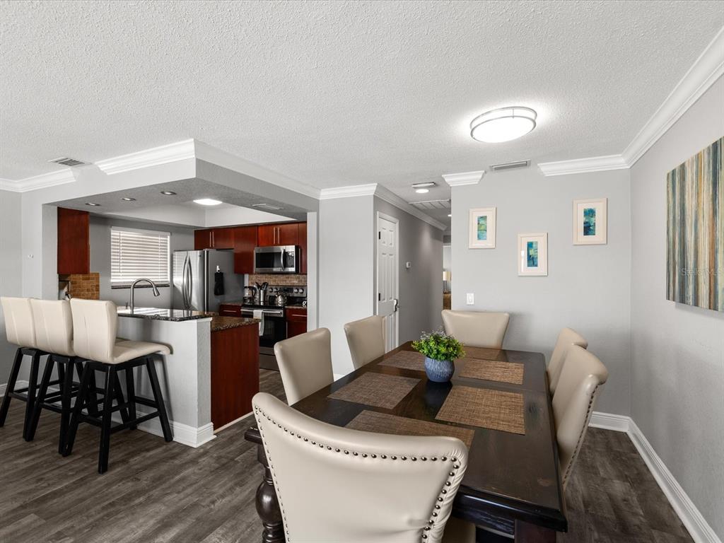 A dining area with a dark wood table and chairs adjacent to an open kitchen — 185 BRIGHTWATER DRIVE UNIT 6, CLEARWATER BEACH, FL