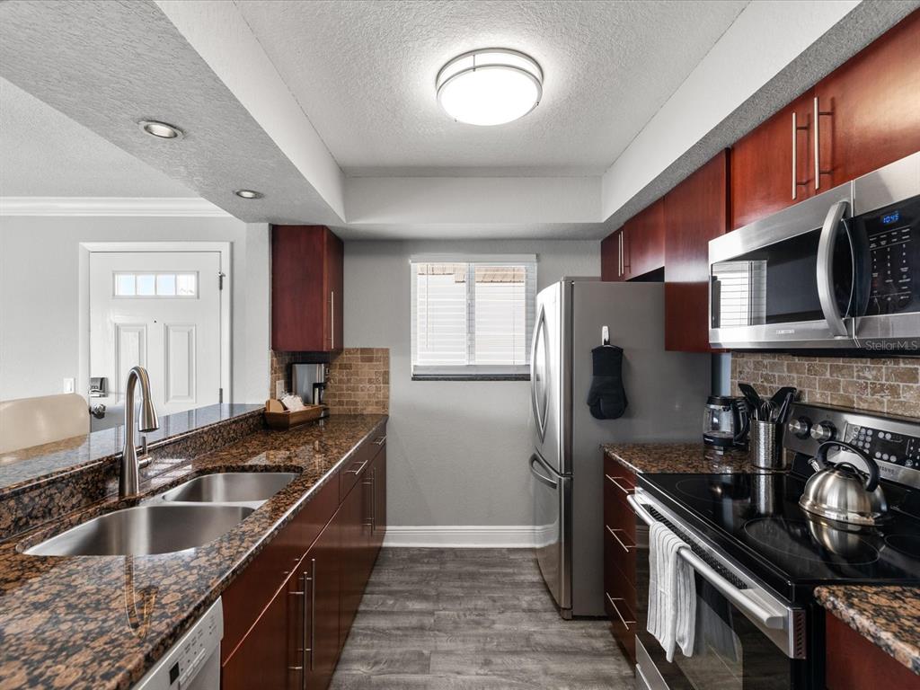 A kitchen features dark wood cabinets, granite countertops, stainless steel appliances, and a tile backsplash — 185 BRIGHTWATER DRIVE UNIT 6, CLEARWATER BEACH, FL