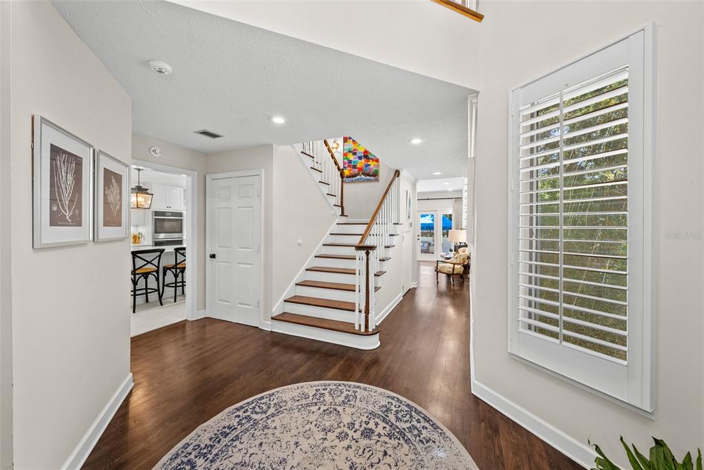 A bright foyer features hardwood floors, a central staircase, and a view into the kitchen — 47 AEGEAN AVENUE, TAMPA, FL