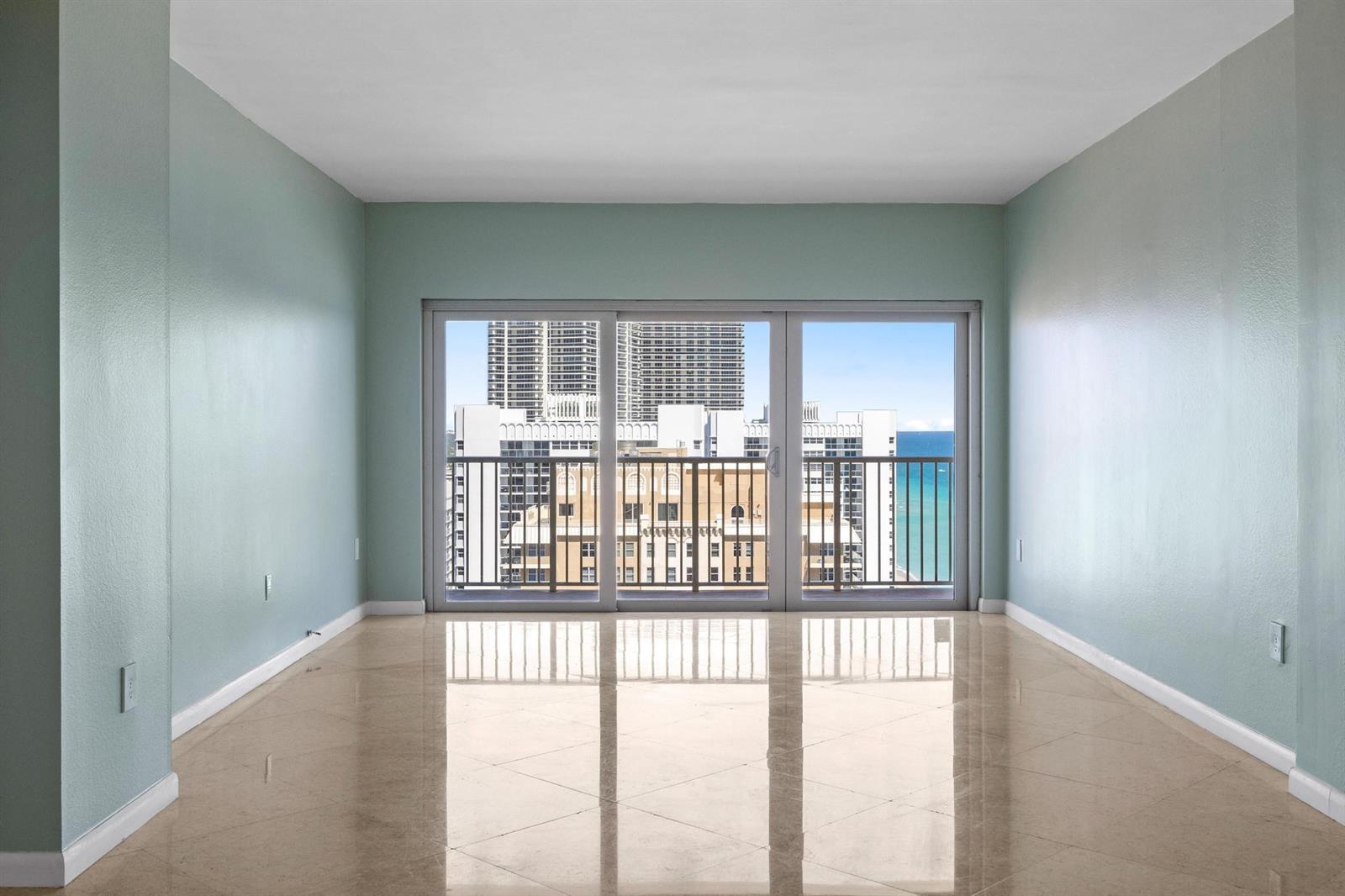 An empty room with light blue walls, polished tile floors, and a sliding glass door — 1950 S Ocean Drive, Hallandale Beach FL 33009, HALLANDALE BEACH, FL
