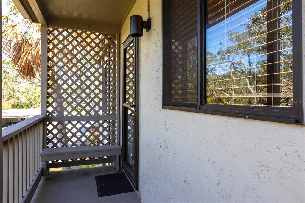 A covered balcony features a wooden bench, lattice privacy screen, and a glass door — 1531 CLOWER CREEK DRIVE UNIT HA245, SARASOTA, FL