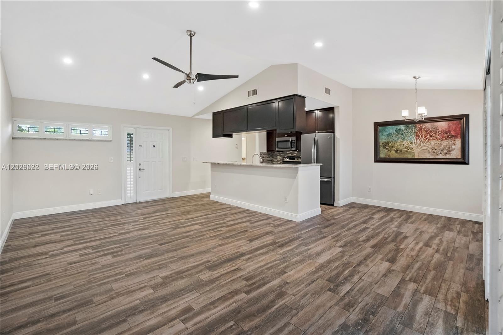 An empty living room features wood-look tile flooring, a vaulted ceiling, and sliding glass doors — 349 NW 94th Ter, Plantation FL 33324, PLANTATION, FL