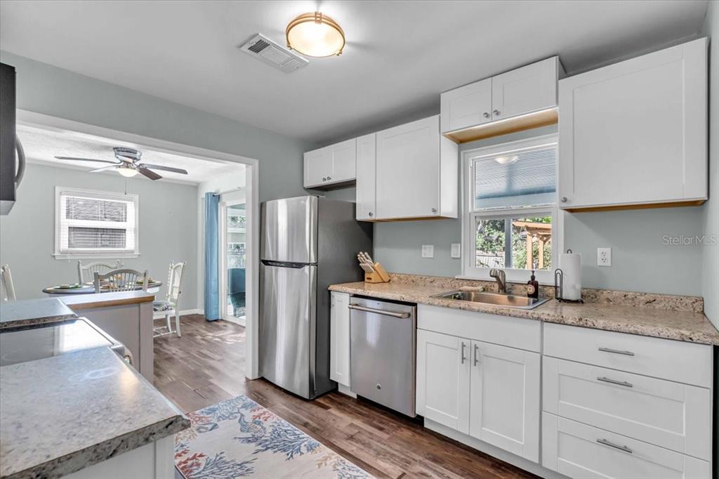 A kitchen with white cabinets, stainless steel appliances, and granite countertops opens to a dining area — 3843 CHAPEL DRIVE, SARASOTA, FL