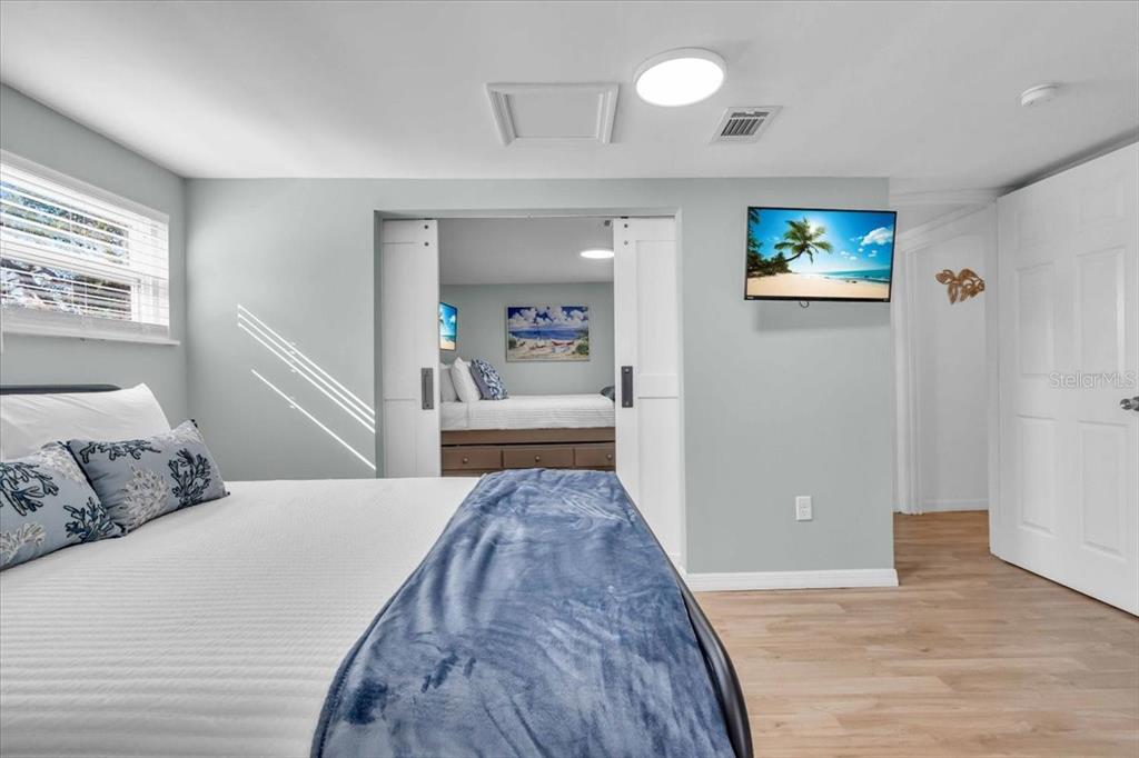 A bedroom features a bed with a blue throw, sliding barn doors, and a wall-mounted television — 3843 CHAPEL DRIVE, SARASOTA, FL