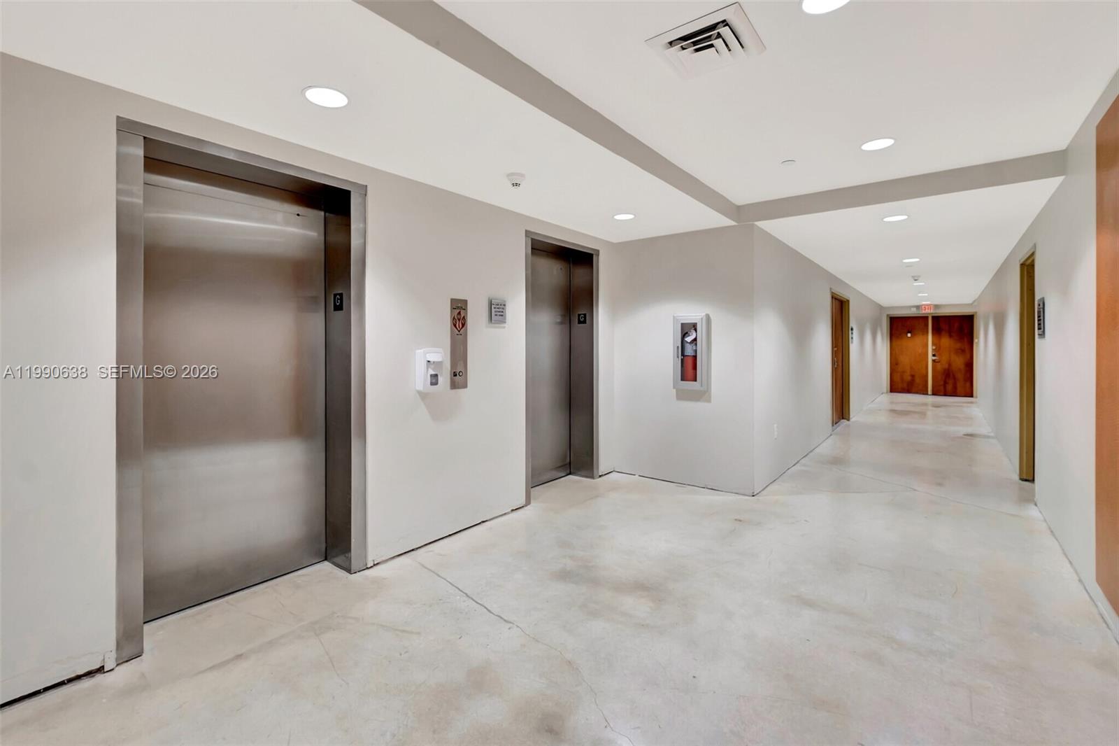 A hallway features two stainless steel elevator doors, a fire extinguisher cabinet, and concrete flooring — 4300 Biscayne Blvd # 202, Miami FL 33137, MIAMI, FL