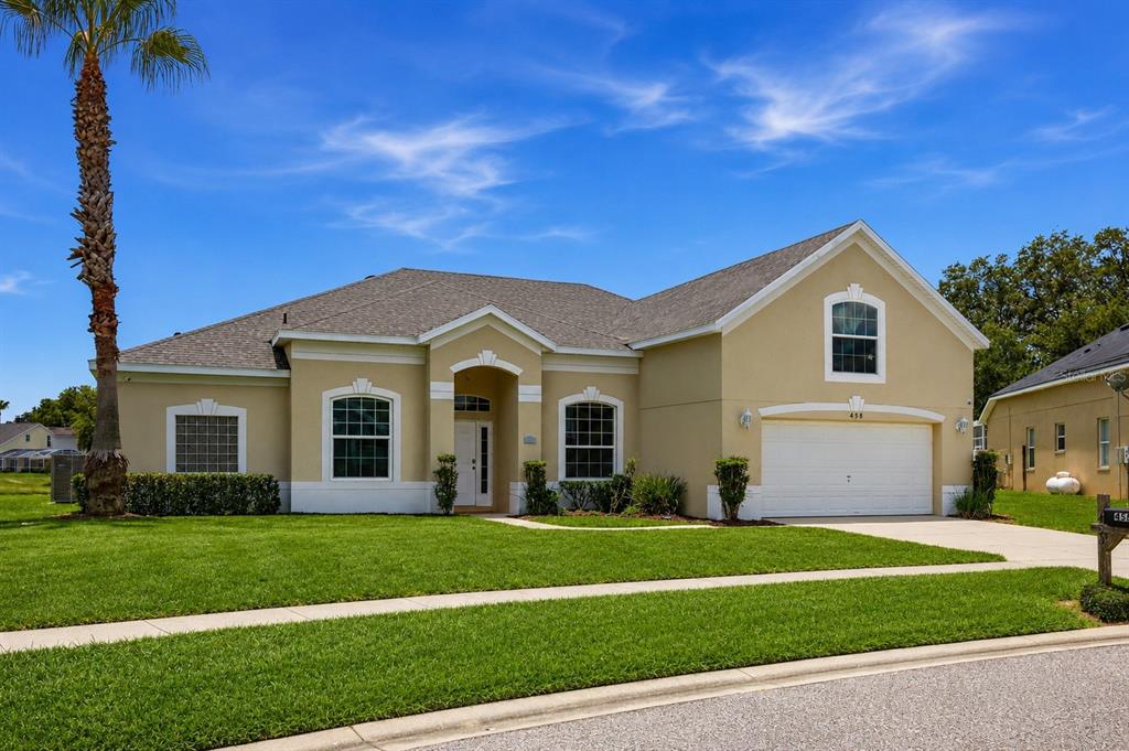 A single-story suburban house with a tan stucco exterior, a two-car garage, and a palm tree — 458 BLOOMINGDALE DRIVE, DAVENPORT, FL