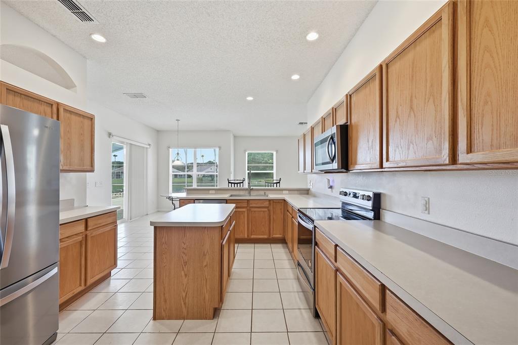 A kitchen with light wood cabinets, white countertops, and tile flooring overlooks a carpeted area — 458 BLOOMINGDALE DRIVE, DAVENPORT, FL