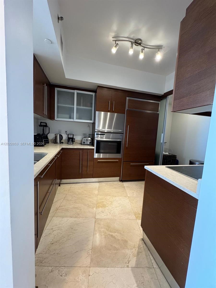 A kitchen features dark wood cabinetry, stainless steel appliances, and light-colored stone flooring — 450 Alton Rd # 3505, Miami Beach FL 33139, MIAMI BEACH, FL