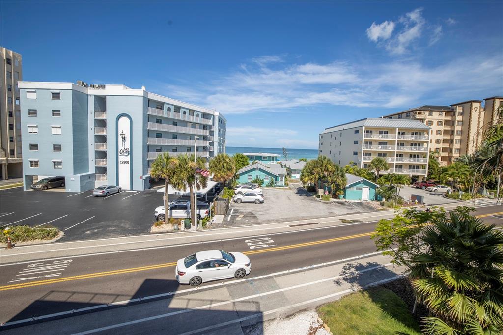 An elevated view shows a street, parking lots, and multi-story apartment buildings near the ocean — 19505 GULF BOULEVARD UNIT 304, INDIAN SHORES, FL
