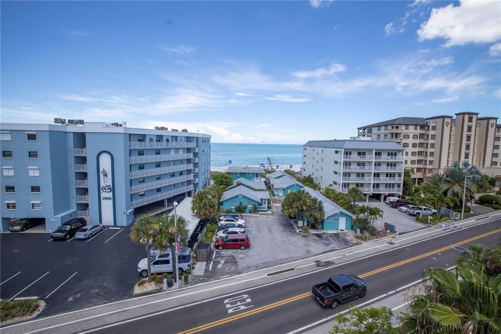 An elevated view shows a coastal street with apartment buildings, parking lots, and the ocean — 19505 GULF BOULEVARD UNIT 304, INDIAN SHORES, FL