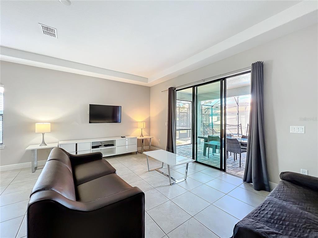 A living room features tile floors, a dark sofa, a media console, and sliding glass doors — 185 BROOKES PLACE, HAINES CITY, FL