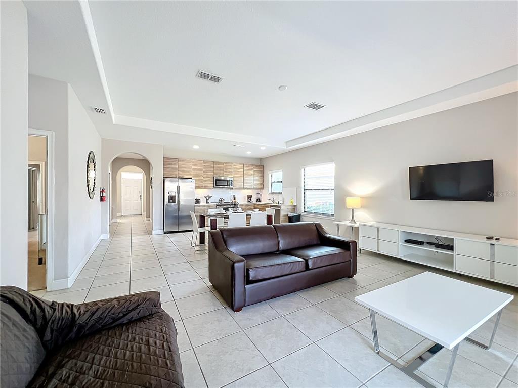 A living room with tile floors, a dark leather sofa, and an open kitchen area — 185 BROOKES PLACE, HAINES CITY, FL