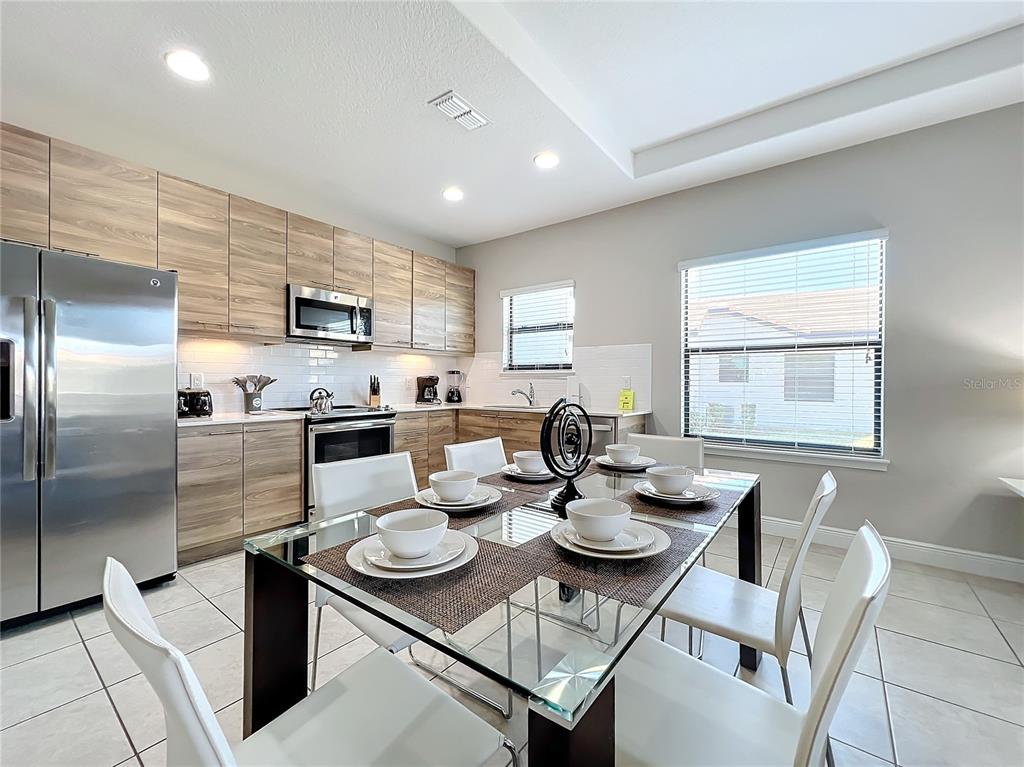 A kitchen with wood-grain cabinets and stainless steel appliances sits adjacent to a glass-topped dining table — 185 BROOKES PLACE, HAINES CITY, FL