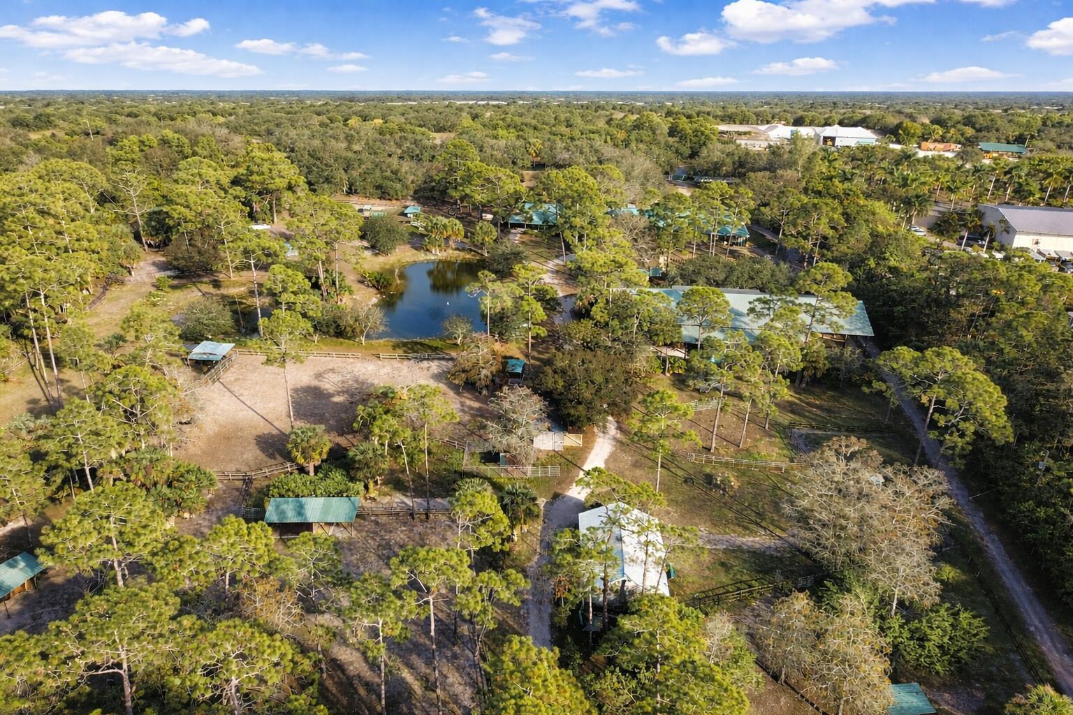 An aerial view shows a wooded property with a pond, several outbuildings, and fenced pastures — 2141 B Road, FL 33470, FL
