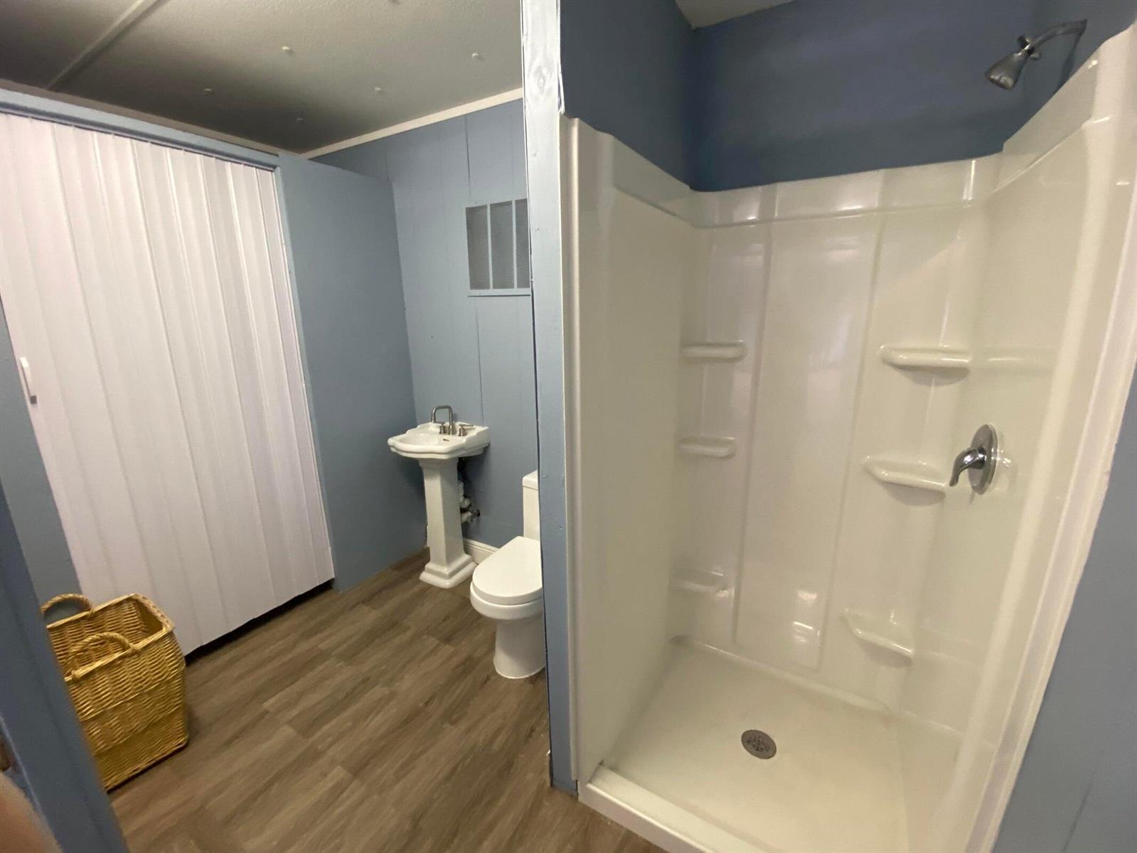 A bathroom features a pedestal sink, toilet, walk-in shower, and wood-look flooring — 2141 B Road, FL 33470, FL
