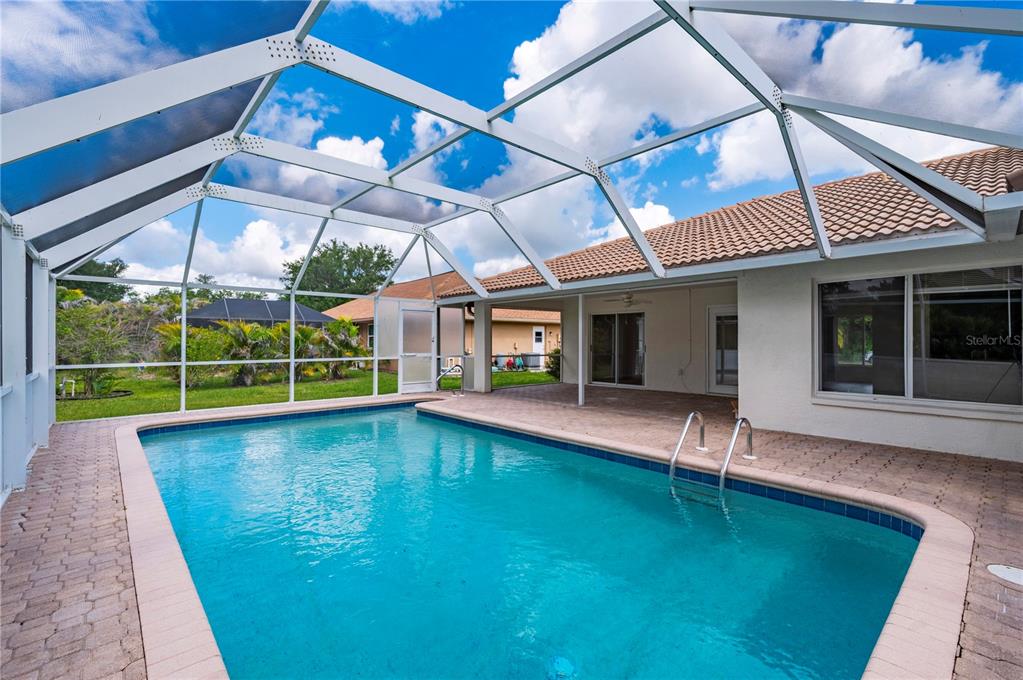 A swimming pool with a screen enclosure sits on a paved patio behind a house — 27055 CHILE DRIVE, PUNTA GORDA, FL