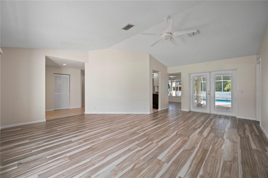 A spacious living room features light wood-look tile flooring, a vaulted ceiling, and glass doors — 27055 CHILE DRIVE, PUNTA GORDA, FL