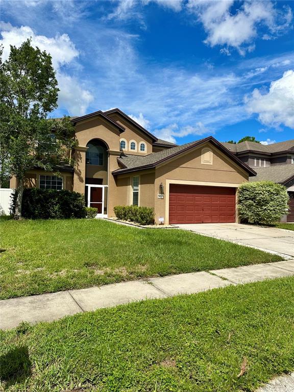 A two-story tan house with a red garage door and a front lawn — 14227 WAKE ROBIN DRIVE, BROOKSVILLE, FL