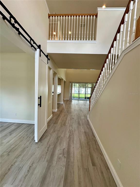 An entryway features wood-look flooring, a white barn door, and a staircase with a railing — 14227 WAKE ROBIN DRIVE, BROOKSVILLE, FL