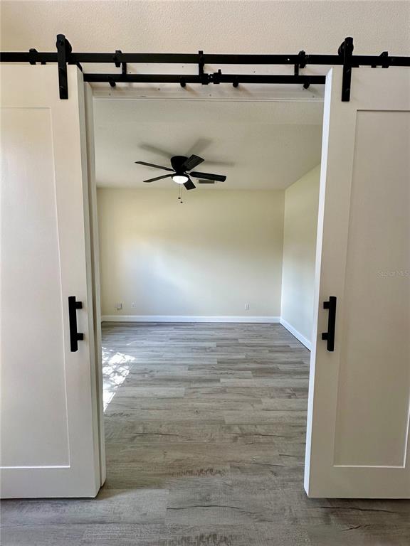 A room with light wood-look flooring and a ceiling fan viewed through white barn doors — 14227 WAKE ROBIN DRIVE, BROOKSVILLE, FL
