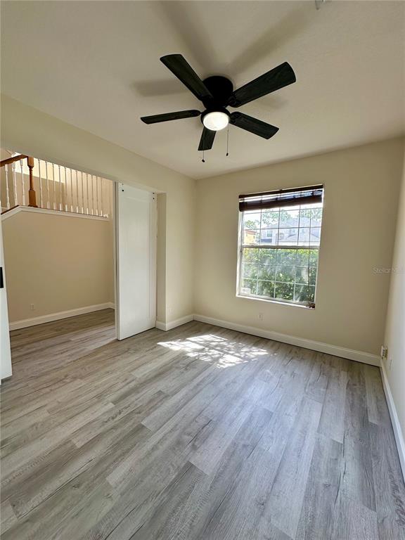 An empty room features light wood-look flooring, a ceiling fan, and a window — 14227 WAKE ROBIN DRIVE, BROOKSVILLE, FL