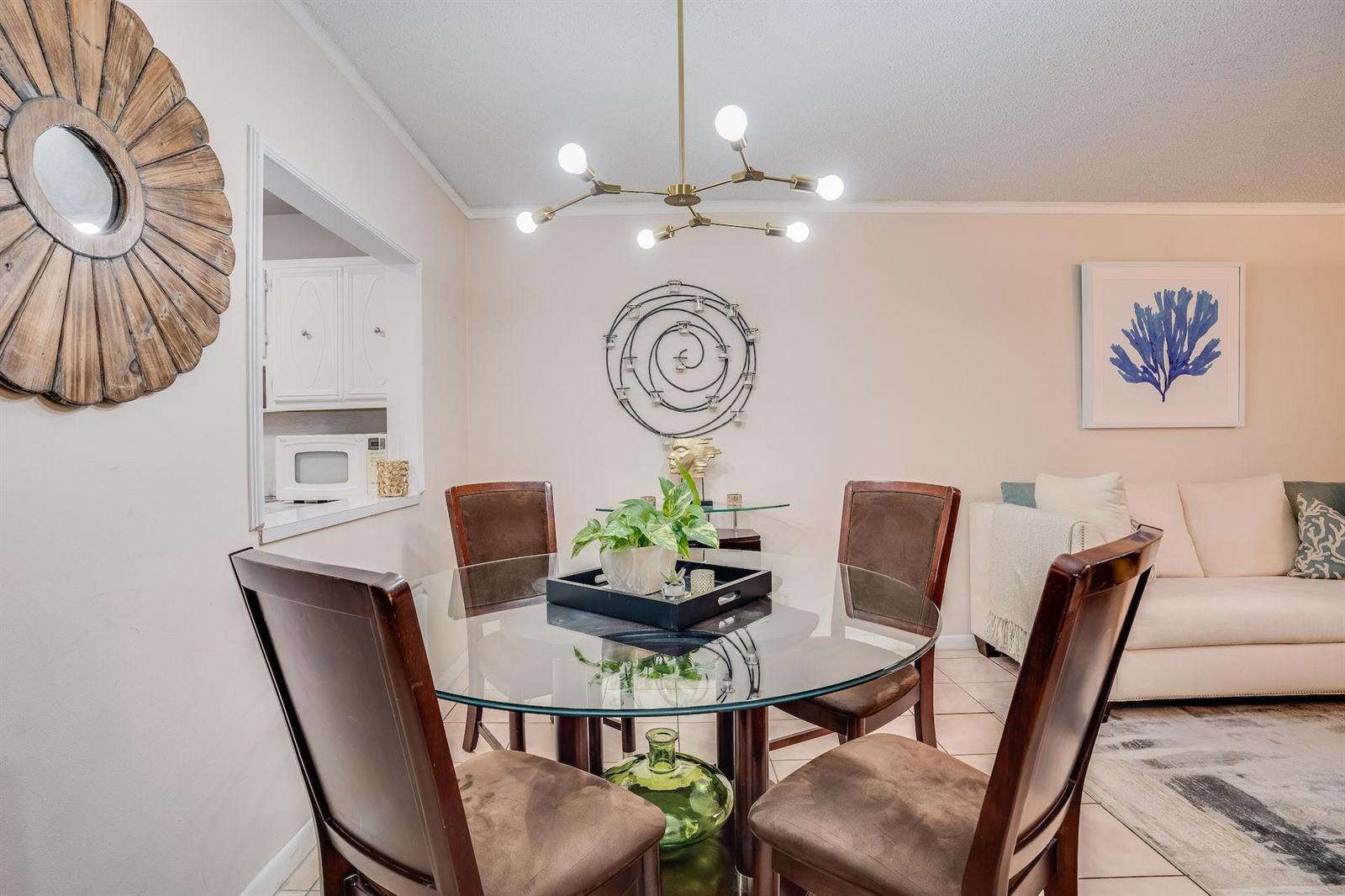 A dining area features a glass-topped table, four brown chairs, and a modern chandelier — 253 S Cypress Road # 202, Pompano Beach FL 33060, POMPANO BEACH, FL