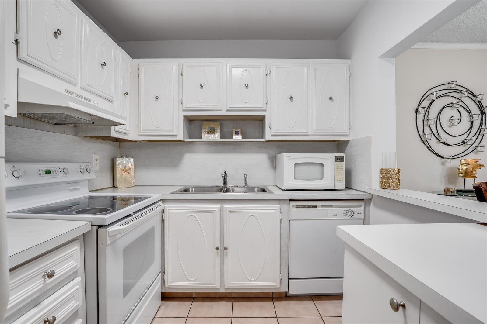 A kitchen features white cabinets, white appliances, a double sink, and light-colored tile flooring — 253 S Cypress Road # 202, Pompano Beach FL 33060, POMPANO BEACH, FL