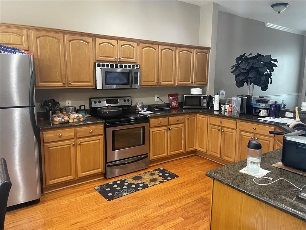 A kitchen features oak cabinets, dark granite countertops, stainless steel appliances, and hardwood flooring — 8405 COSTA BELLA WAY, TEMPLE TERRACE, FL