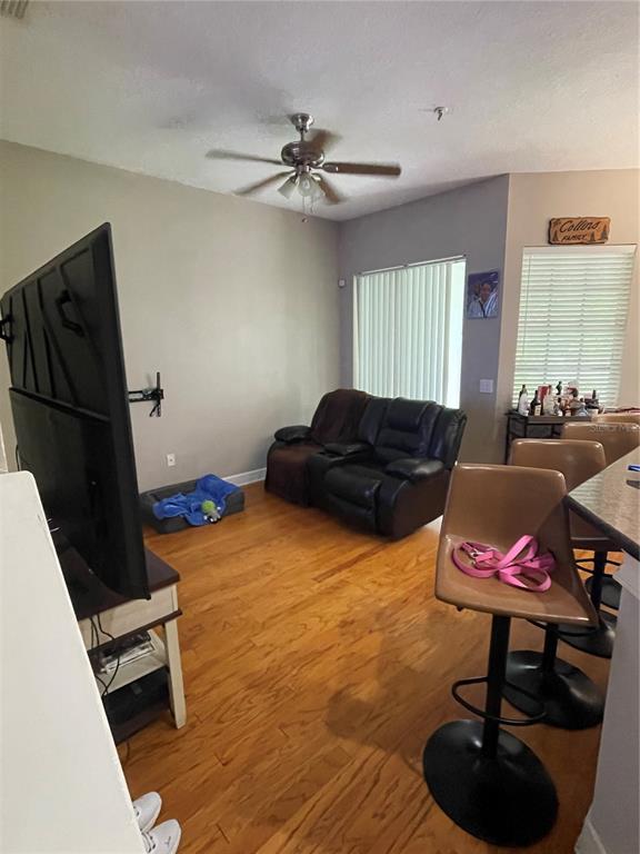 A living room features hardwood floors, a ceiling fan, a television, and a leather loveseat — 8405 COSTA BELLA WAY, TEMPLE TERRACE, FL
