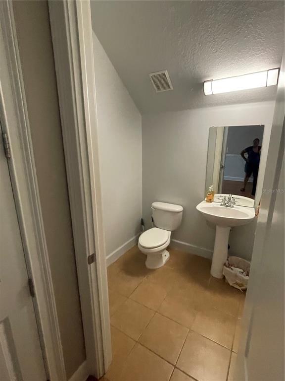 A half bathroom features a pedestal sink, a toilet, and light-colored tile flooring — 8405 COSTA BELLA WAY, TEMPLE TERRACE, FL