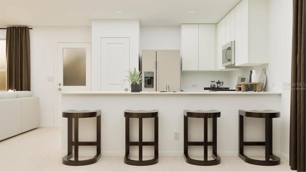 A kitchen with white cabinets, stainless steel appliances, and four dark stools at a counter — 7722 MARBLE STREET, GROVELAND, FL