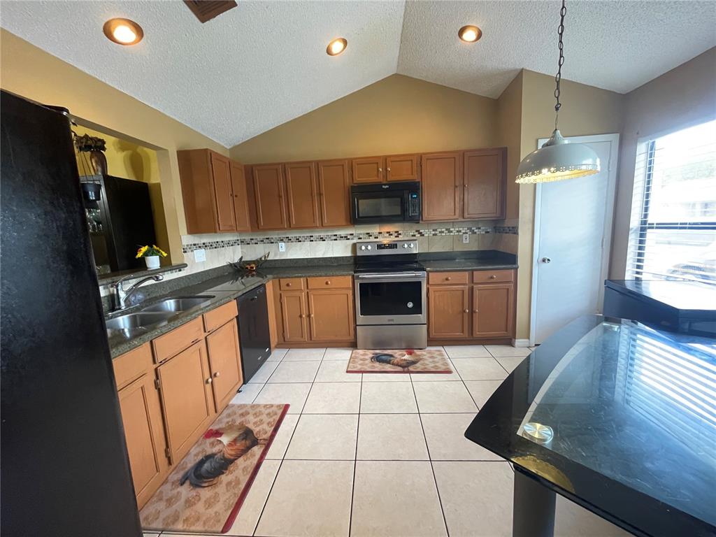 A kitchen features wood cabinets, stainless steel appliances, tile flooring, and a vaulted ceiling — 3050 GOLDEN ROCK DRIVE, ORLANDO, FL