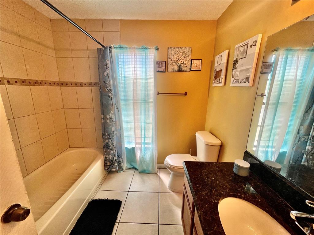 A bathroom features a tiled shower-tub combo, a toilet, and a dark countertop vanity — 3050 GOLDEN ROCK DRIVE, ORLANDO, FL