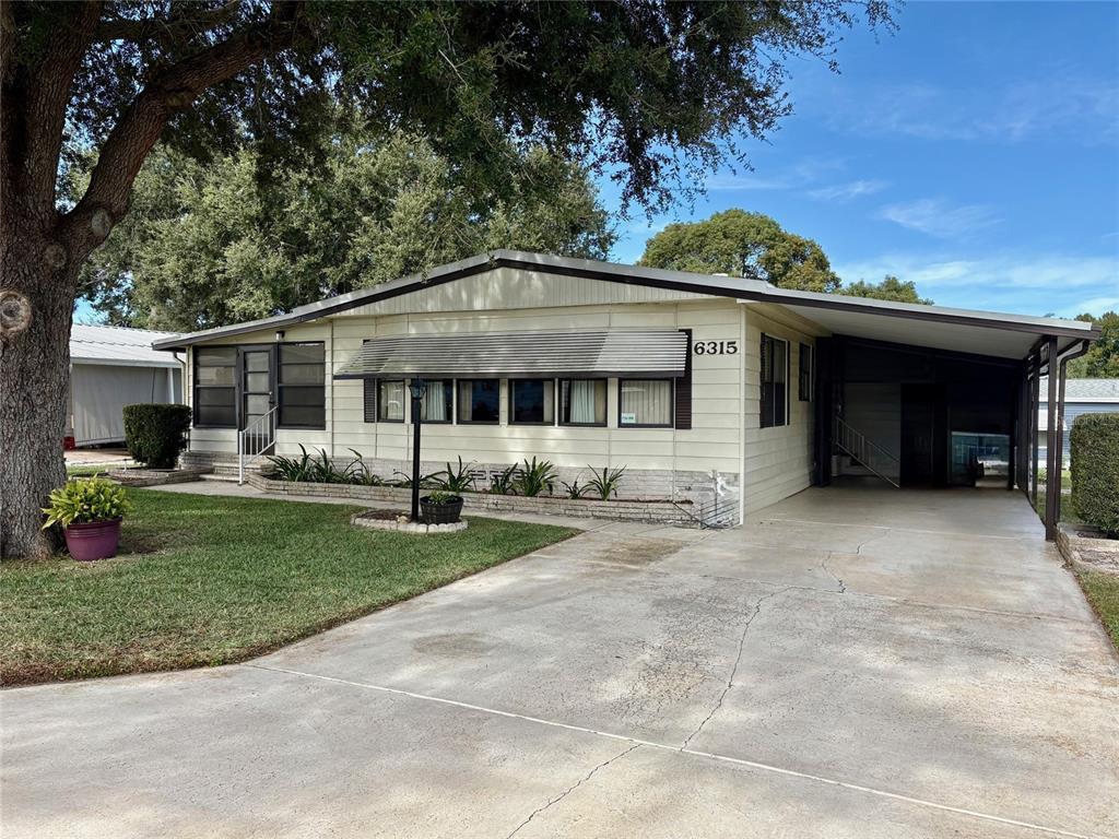 A single-story manufactured home features light siding, a metal awning, and an attached carport — 6315 GROVE POINTE DRIVE SE, WINTER HAVEN, FL