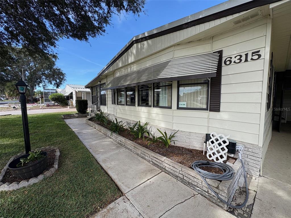 The exterior of a mobile home features light-colored siding, a brick planter, and a walkway — 6315 GROVE POINTE DRIVE SE, WINTER HAVEN, FL