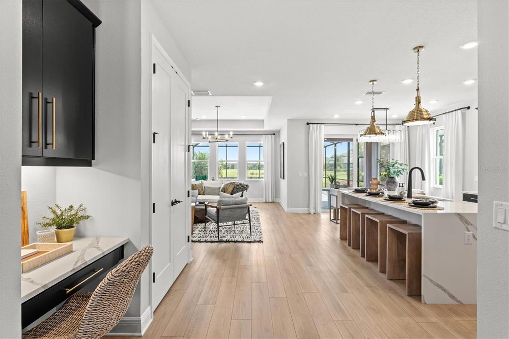A modern open-concept kitchen and living area features light wood floors and a built-in desk — 4719 WINSOME WAY, BRADENTON, FL