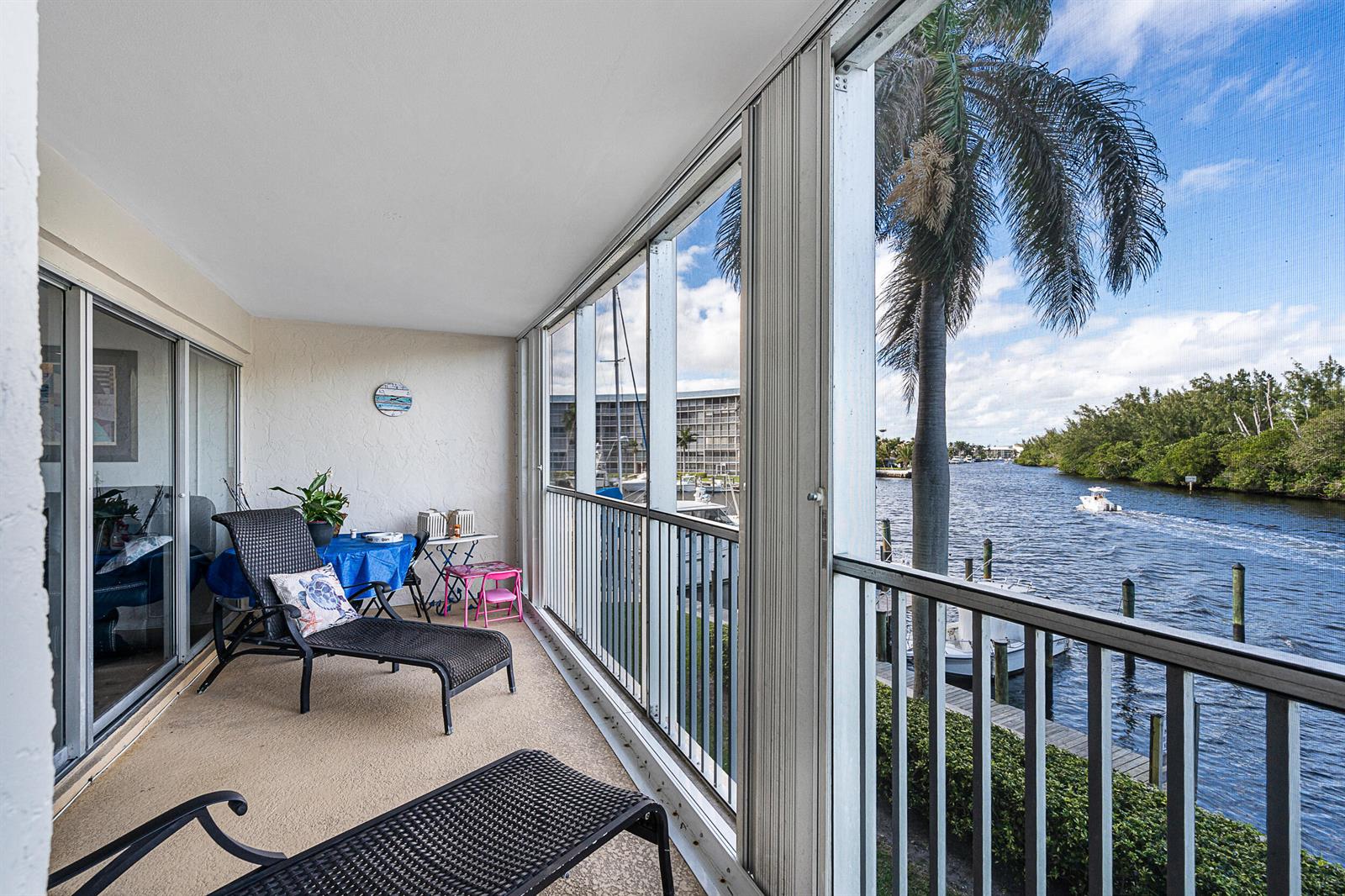 A screened-in balcony overlooks a canal with a boat and palm tree — 1537 E Hillsboro Boulevard # 243, Deerfield Beach FL 33441, DEERFIELD BEACH, FL